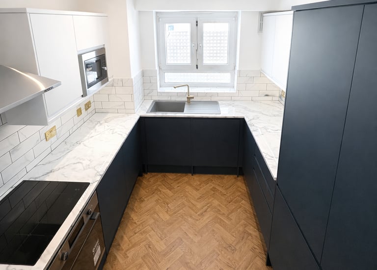 Modern kitchen with navy blue cabinets, white marble countertops, and herringbone wood flooring.