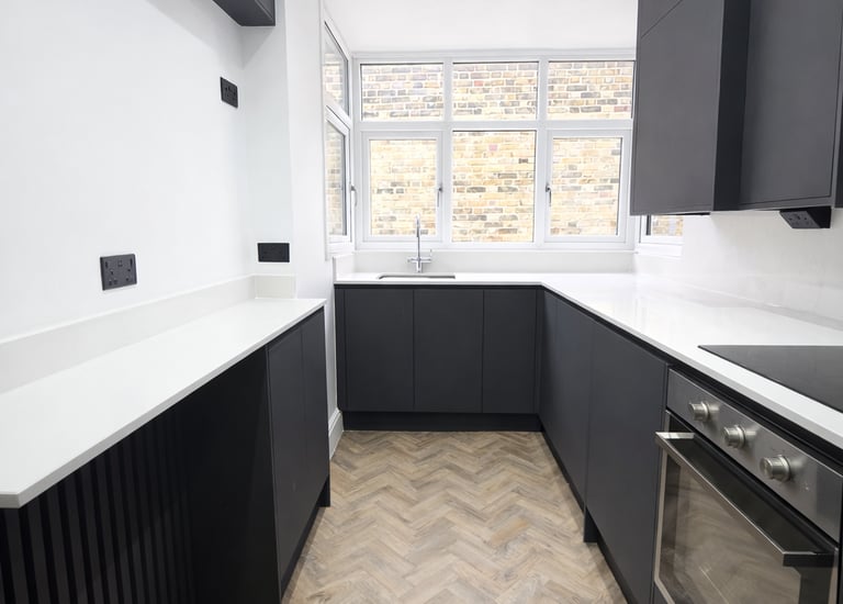 Modern narrow kitchen featuring charcoal cabinets, white quartz countertops, and herringbone flooring.
