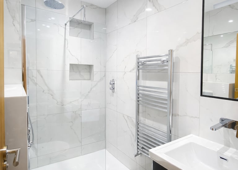 Modern bathroom with white marble tiles, walk-in shower, vanity unit, and heated towel rail.