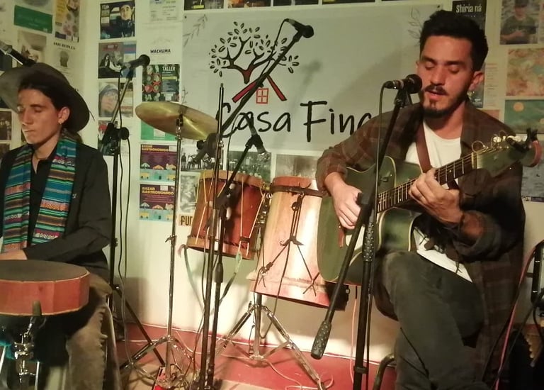 Dos músicos interpretando música folclórica en vivo con una guitarra acústica y un tambor de mano 