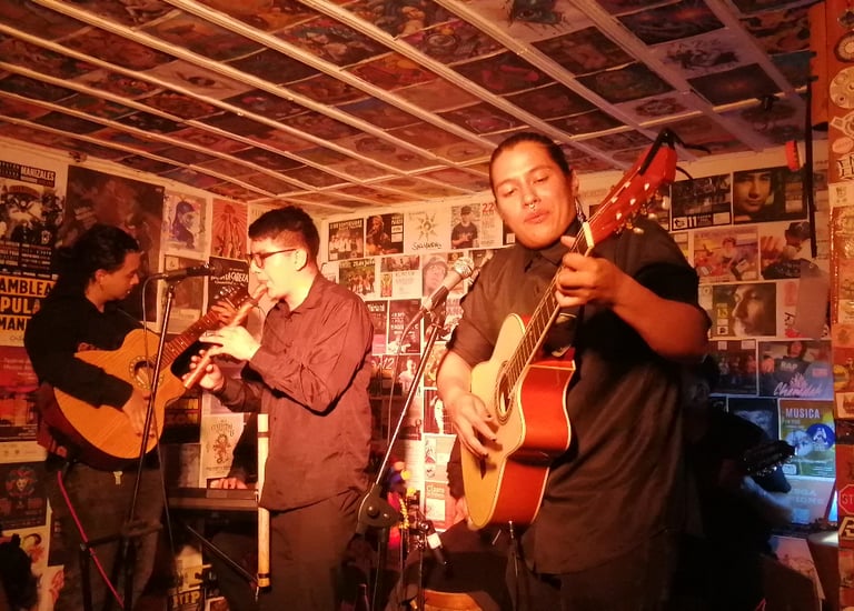 Tres músicos se presentan en el escenario con guitarras acústicas y una flauta, en un espacio lindo