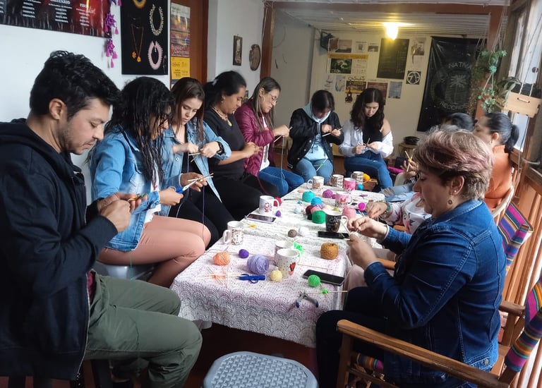 Personas concentradas al rededor de una mesa con hilos, herramientas y bebidas calientes, elaborando mandalas tejidos