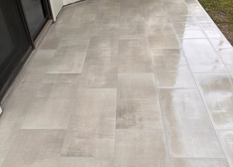 Modern outdoor patio with large grey porcelain tiles installed next to a sliding glass door.