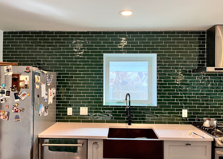 Modern kitchen featuring a dark green subway tile backsplash and a black farmhouse sink with white countertops.