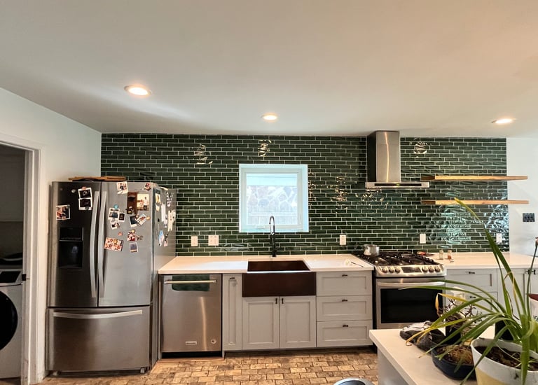Modern kitchen featuring a green subway tile backsplash, white cabinets, and stainless steel appliances.