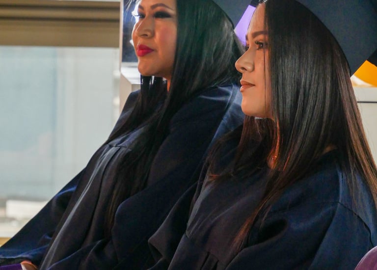 Dos mujeres graduadas que visten togas y birretes académicos de color azul marino en una ceremonia d