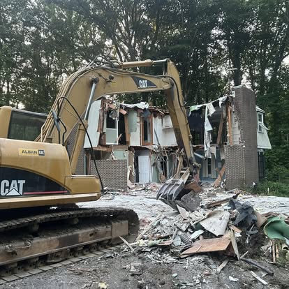 Yellow CAT excavator clearing debris during a residential house demolition project.