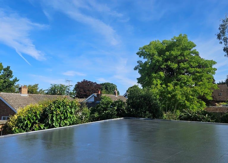 A waterproof grey flat roof installation on a residential house under a clear blue sky.