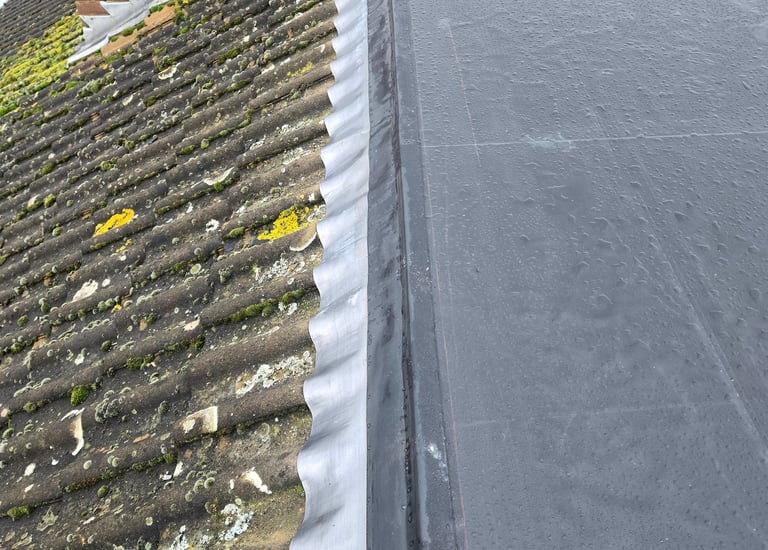 Black EPDM rubber flat roof installation with lead flashing connected to a traditional tiled roof.