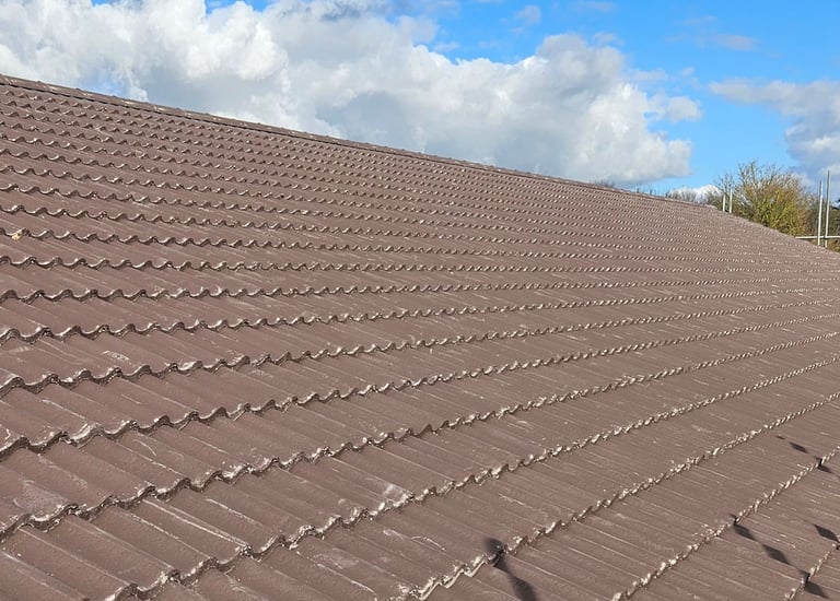 Durable brown concrete roof tiles installed on a residential home under a blue cloudy sky.