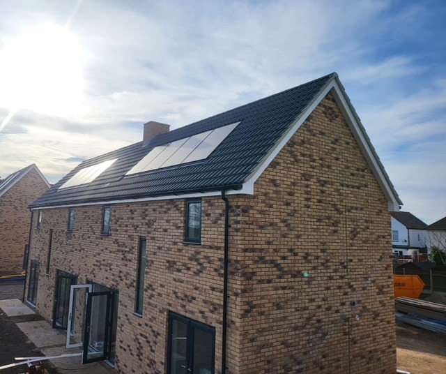 Modern brick house with rooftop solar panels installed on a dark tiled roof under a bright blue sky.