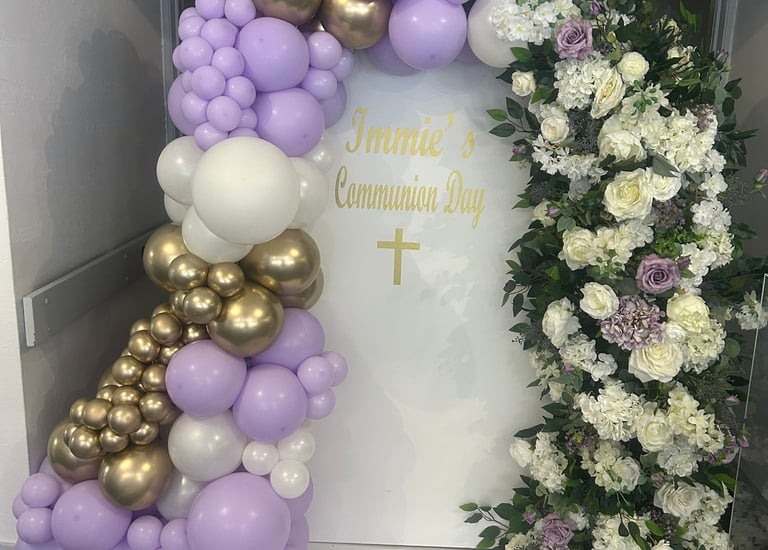 Purple, white, and gold balloon arch with floral backdrop for a First Holy Communion celebration.