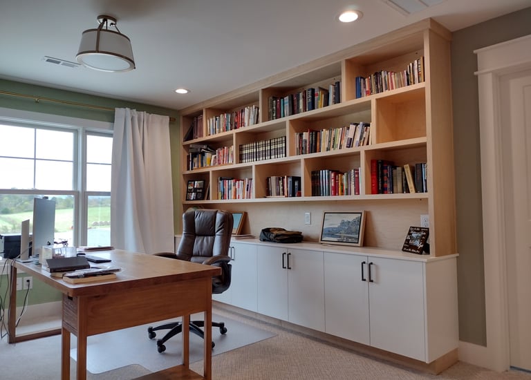 Modern home office featuring a large wood desk and custom built-in bookshelves with white cabinets.