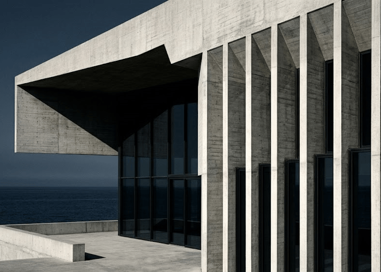 Modern brutalist concrete building with vertical pillars and glass walls overlooking the ocean.