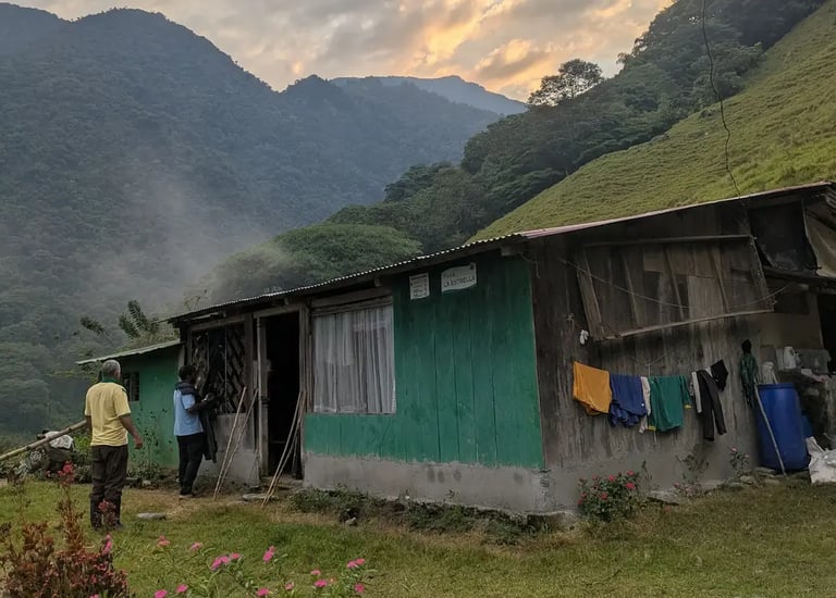 Rustic green wooden farmhouse in a tropical mountain valley with laundry hanging and misty peaks.