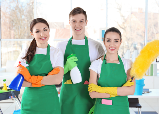 a group of people in green aprons holding cleaning supplies