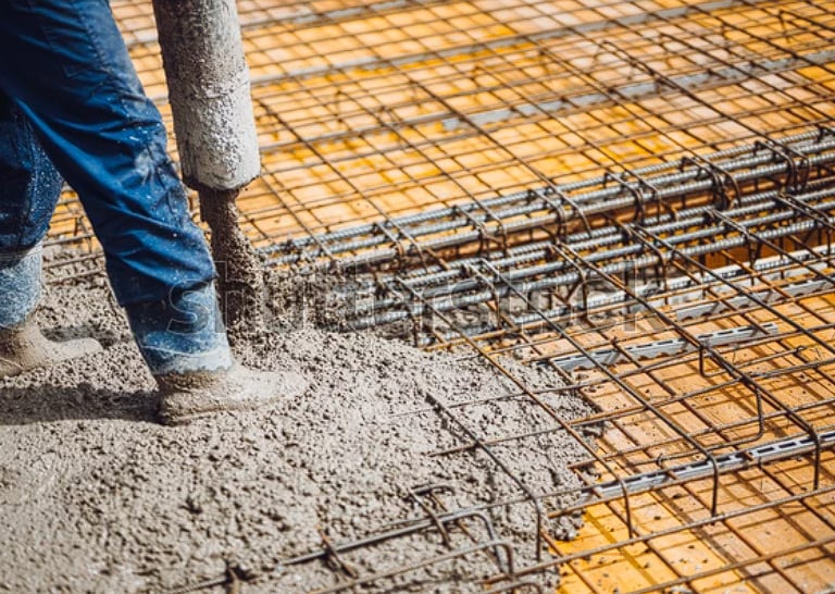 Worker holding concrete pumping hose over wire mesh.
