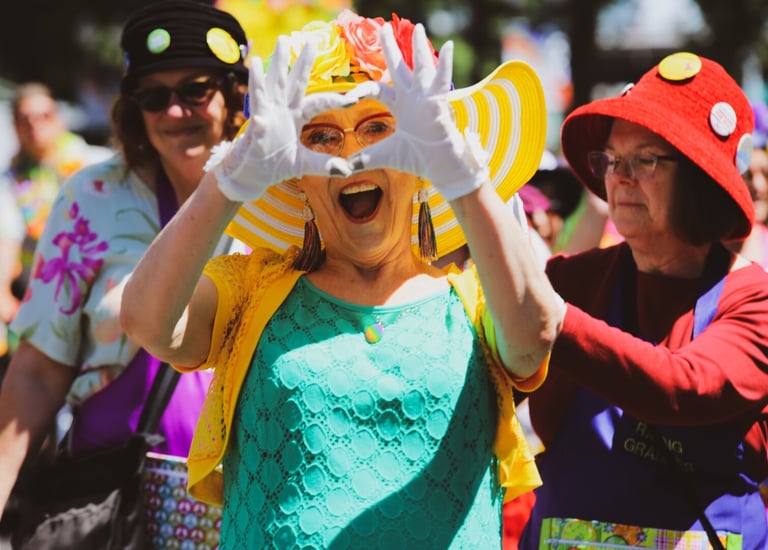 a woman in a green dress with a yellow hat makes a finger heart in front of her face
