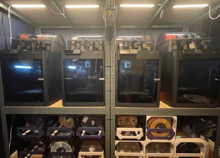 a shelf with a 4 bambu p1s printers. A bunch of filament rolls on the bottom of the shelves