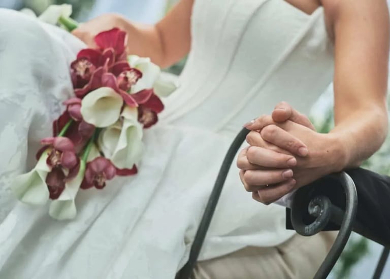 A close-up shot of a bride in a white gown holding a bouquet of burgundy orchids and white calla lilies
