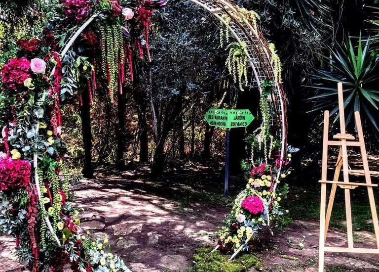 A large circular arch decorated with vibrant pink and red flowers and lush greenery in a garden setting