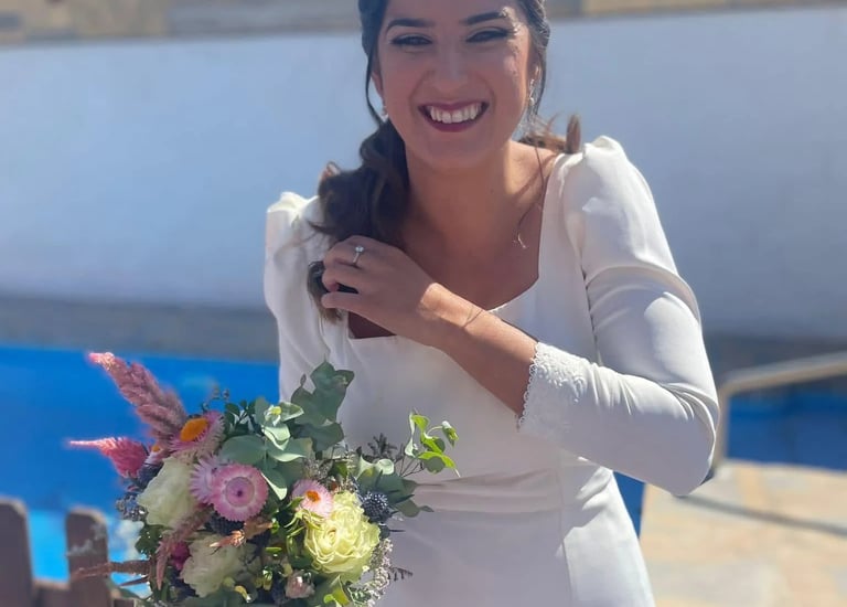 A happy bride in a white wedding dress, smiling and holding a colorful flower bouquet