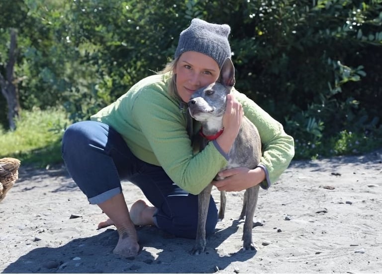 a woman in a green sweater with a dog on the beach