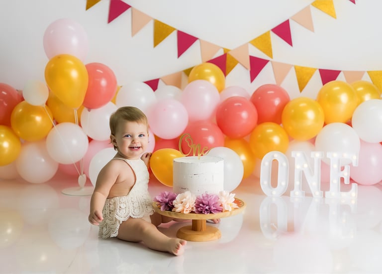 bebé sentada junto a tarta delante de globos en la sesión de smash cake