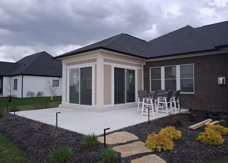 New patio enclosure finished with panel siding and white trim around two sliding glass doors.