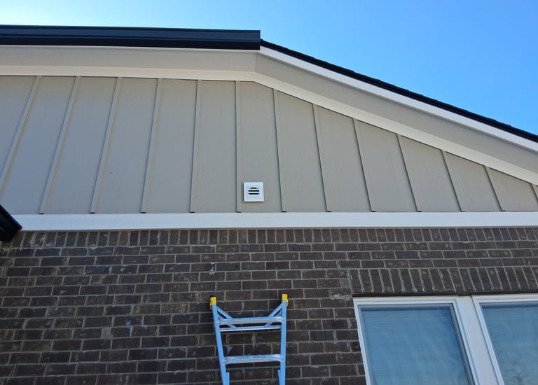 Board and batten style siding on gable end of a house above red brick.