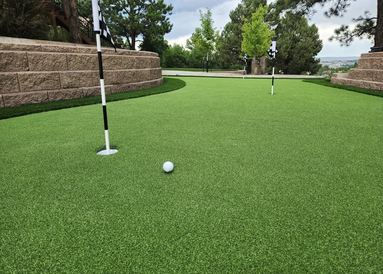 an artificial putting green area with fringe around it and a golf ball and cup and flag.