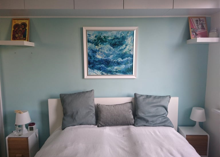 a bed with a white bed and a blue sea painting on the wall