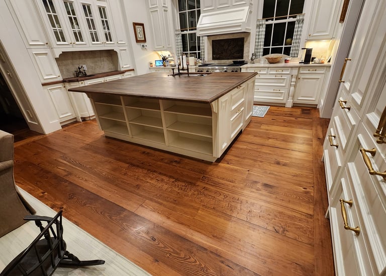 Luxury kitchen featuring wide plank heart pine hardwood floors and a large white center island with a wood countertop.