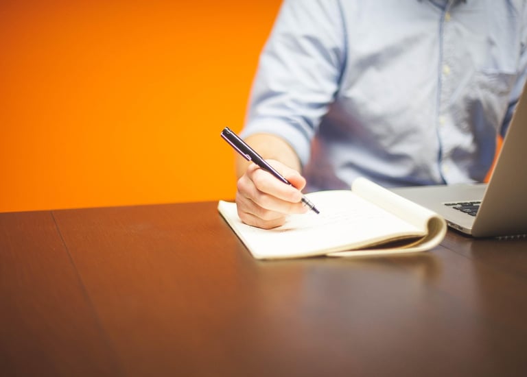 orange background with a man's torso seated at a desk holding a pen and taking notes