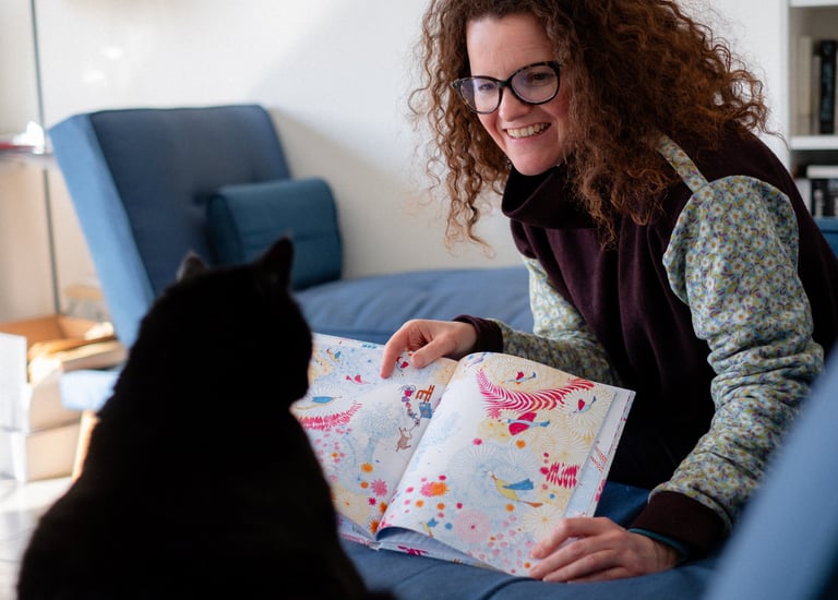 Une illustratrice qui montre son livre jeunesse à son chat noir