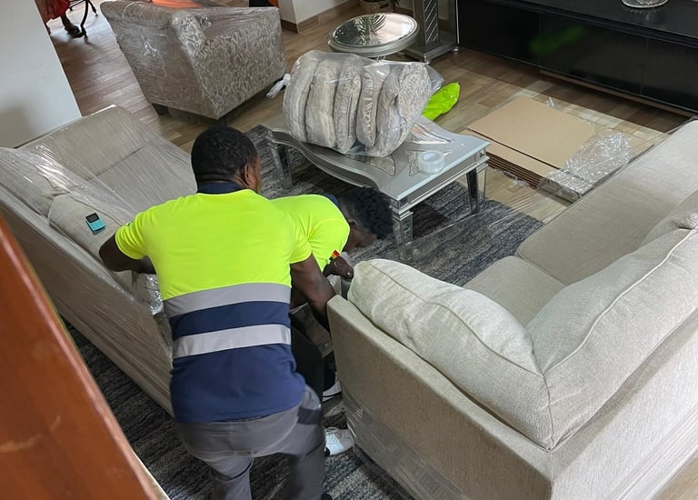 A professional mover in a yellow high-visibility vest with blue stripes bends over to wrap a large b