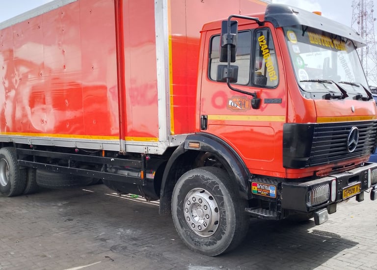 A vibrant red Mercedes-Benz delivery truck with a white enclosed cargo box, yellow and orange accent