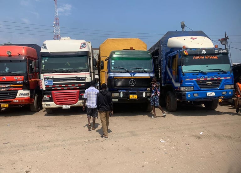 A row of colorful heavy-duty trucks—red MAN, white DAF, yellow flatbed, and blue DAEWOO—parked side 