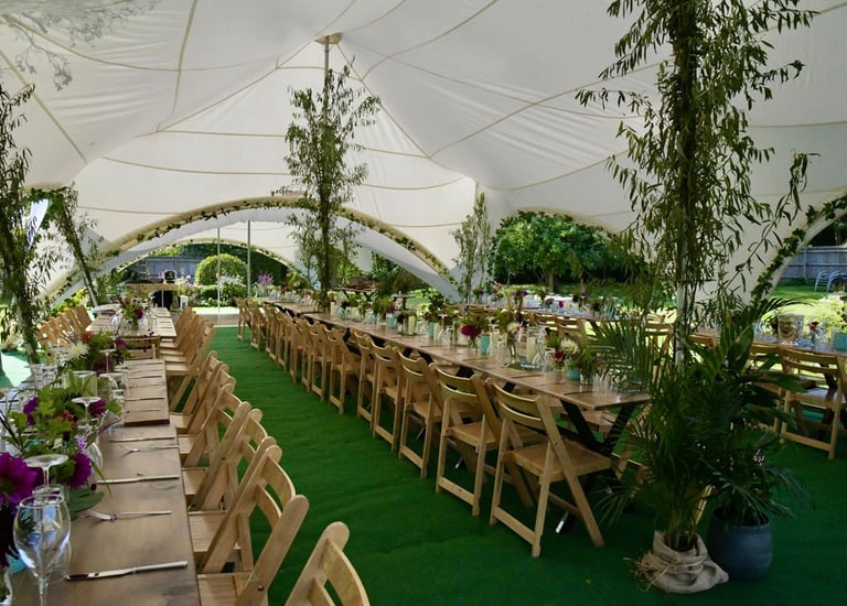 Rustic outdoor wedding reception inside a white marquee tent with long wooden tables and green turf.
