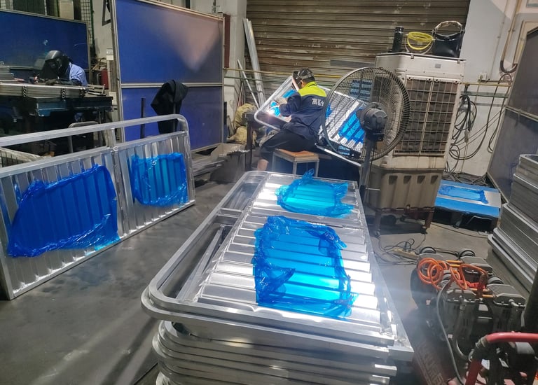 Professional welders fabricating aluminum frames in an industrial metal manufacturing workshop.