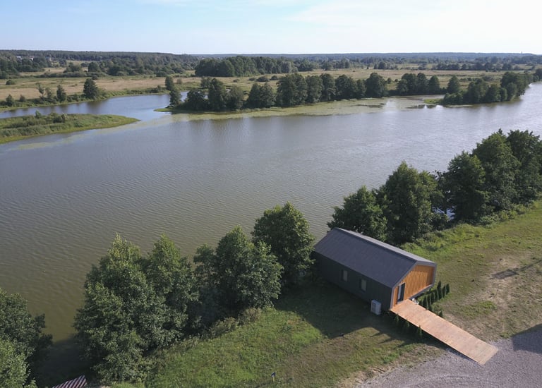 Aerial view of a modern tiny house cabin on a lakefront with a wooden walkway.