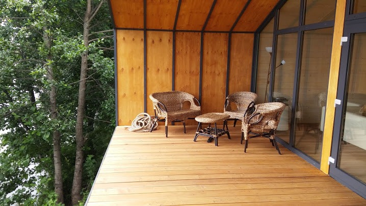 Modern wooden balcony with wicker chairs overlooking a lush green forest.