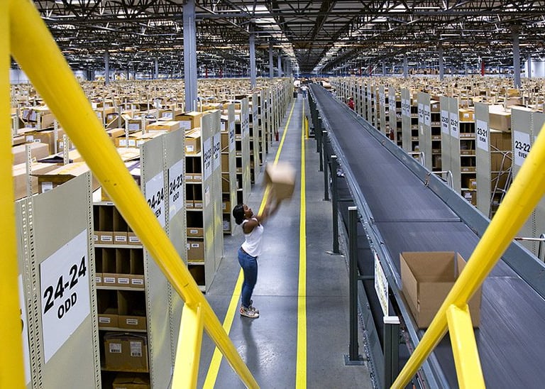 A worker sorting cardboard boxes on a conveyor belt system inside a large distribution warehouse center.