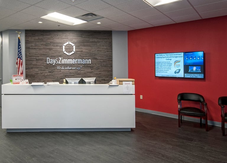 Modern office reception area for Day & Zimmermann with white desk and stone accent wall.