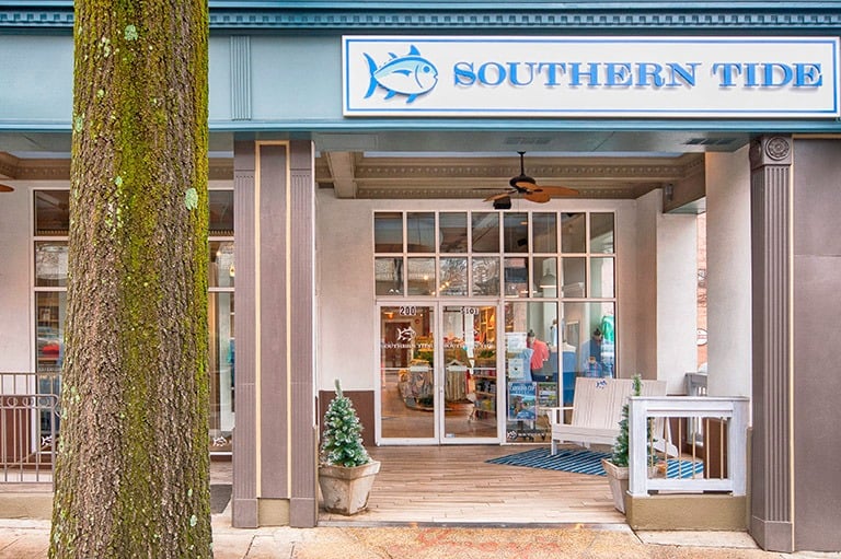 Southern Tide storefront entrance with blue brand signage and outdoor seating area.