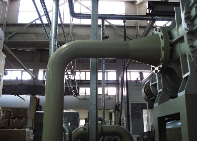 Industrial HVAC ventilation system with large metal pipes and ductwork in a warehouse.