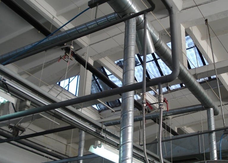 Industrial ceiling with metal HVAC air ducts, ventilation pipes, and factory skylights.