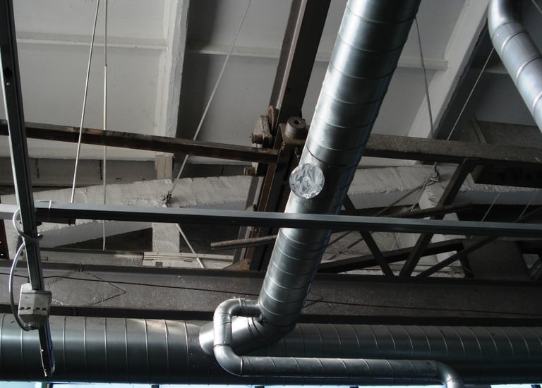 Industrial HVAC spiral ductwork and ventilation pipes installed on a warehouse ceiling.