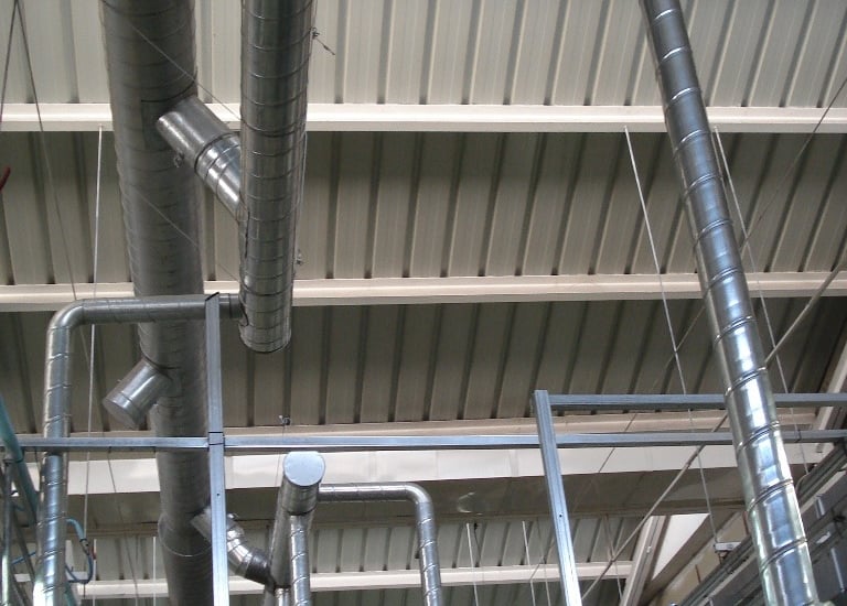Industrial HVAC spiral ductwork and ventilation pipes installed along a high warehouse ceiling.