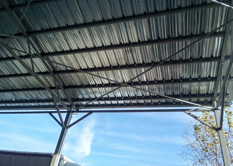 Underside of a modern metal carport roof with steel frame trusses against a blue sky.